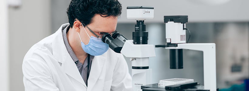 Scientist in the lab looking through a microscope while participating in live virtual training on the neural differentiation of pluripotent stem cells.