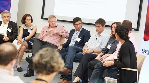 The eight panel speakers are shown engaged in discussion on stage.
