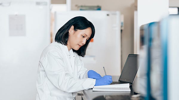 User taking notes while using a laptop to take a free, self-paced virtual training course.